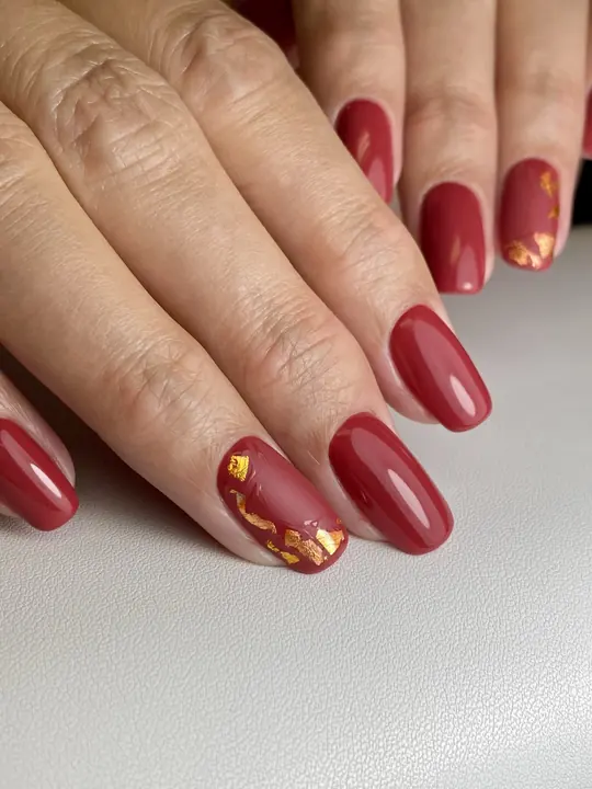 Deep burgundy gel manicure with gold foil accents